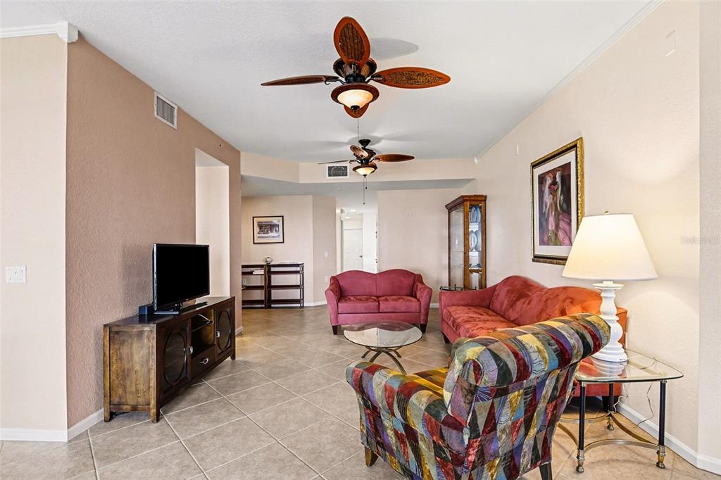 A living room features tile flooring, two ceiling fans, and a mix of colorful furniture — 4696 CLUB DRIVE UNIT 102, PORT CHARLOTTE, FL