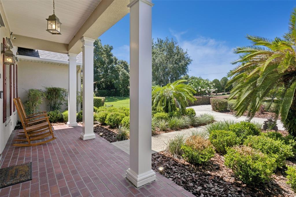A covered brick porch features white columns, two wooden rocking chairs, and a landscaped yard — 605 OLD MOUNT DORA ROAD, EUSTIS, FL