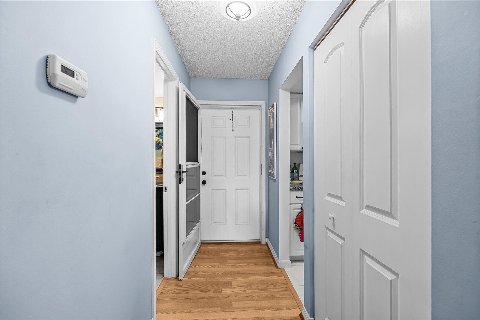 A hallway with light blue walls, wood flooring, a white front door, and closet doors — 1943 SW Palm City Road # d, Stuart FL 34994, STUART, FL
