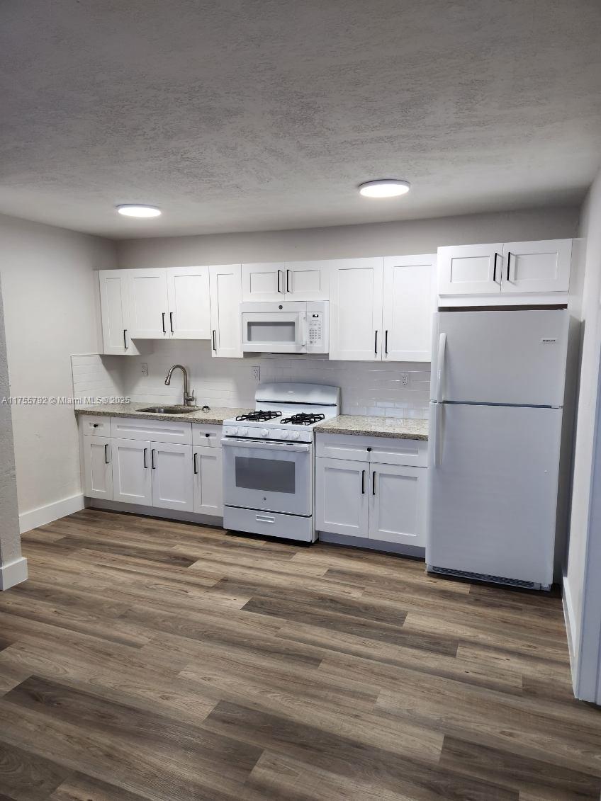 A kitchen features white cabinets, stainless steel appliances, granite countertops, and wood-look flooring — 25 W 6th St # 25, Hialeah FL 33010, HIALEAH, FL