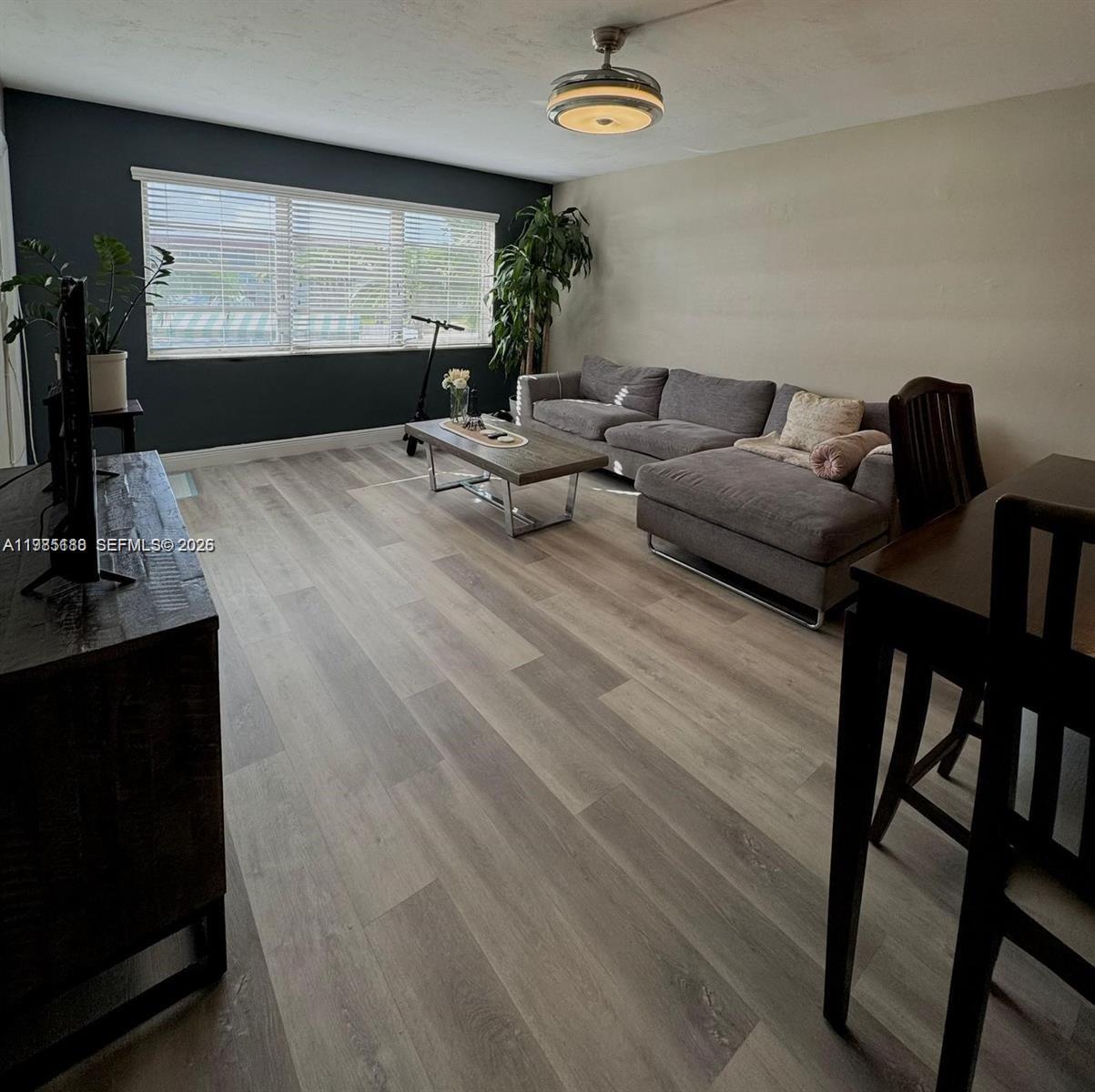 A living room features gray wood-look flooring, a sectional sofa, and a dark accent wall — 1530 NE 191st St # 241, Miami FL 33179, MIAMI, FL