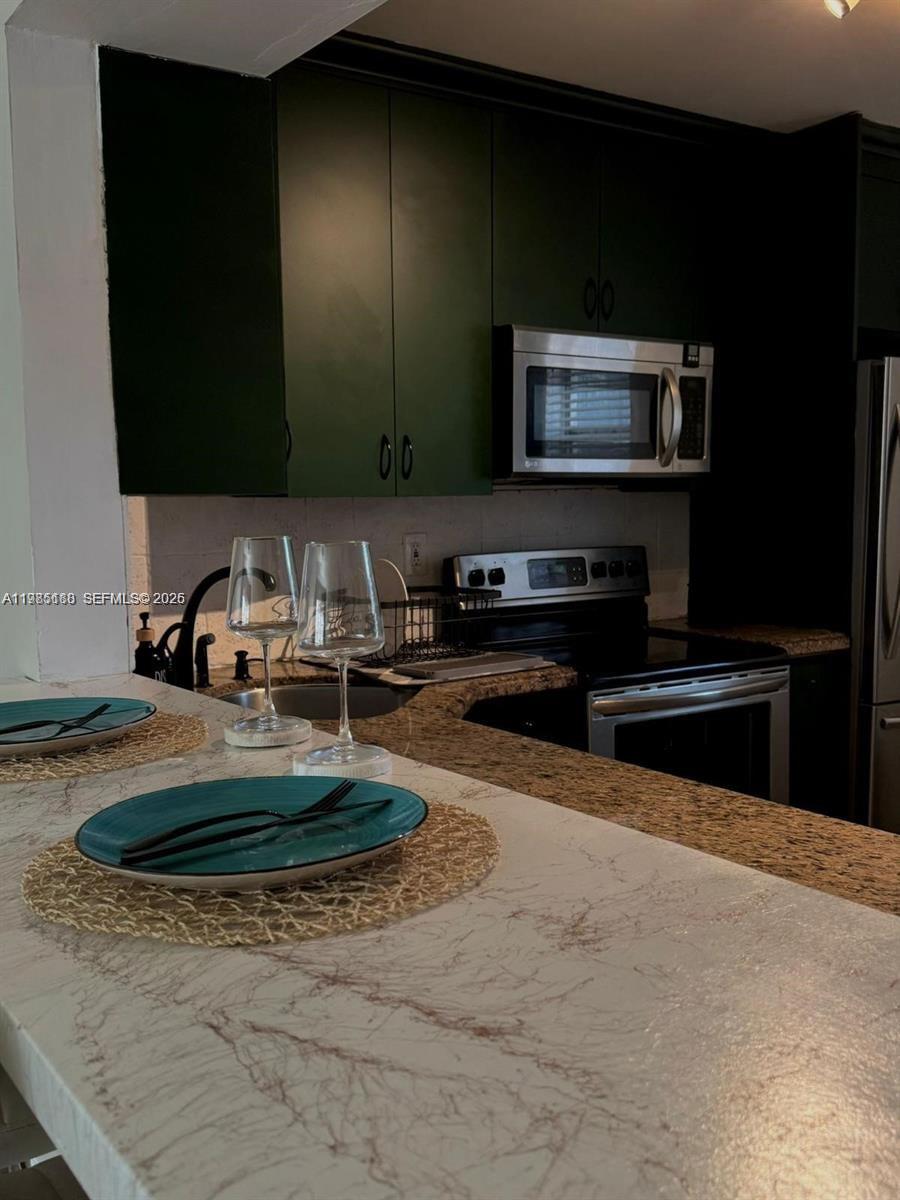 A kitchen features dark green cabinets, granite countertops, and a breakfast bar with place settings — 1530 NE 191st St # 241, Miami FL 33179, MIAMI, FL
