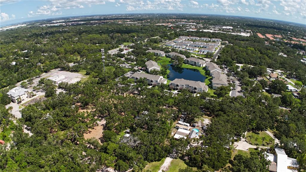 An aerial view shows apartment buildings surrounding a pond amidst a wooded suburban landscape — 0 51ST STREET, SARASOTA, FL