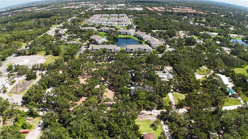 An aerial view shows a wooded lot adjacent to a multi-building apartment complex with ponds — 0 51ST STREET, SARASOTA, FL