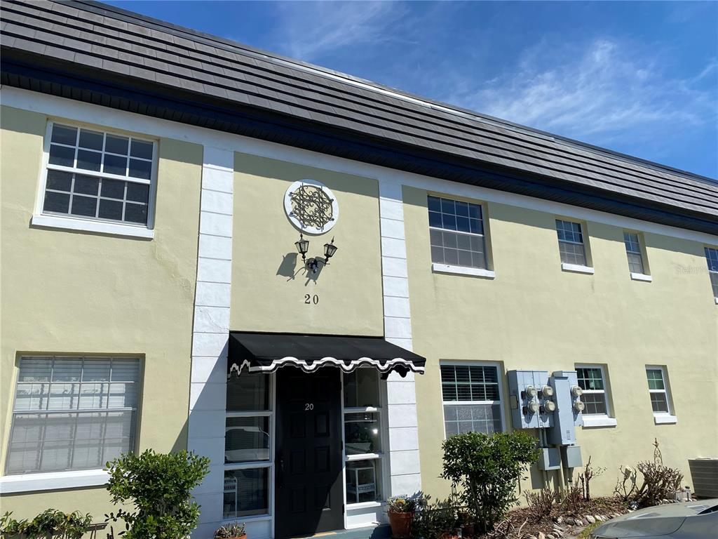 A two-story building exterior features light yellow stucco walls, a dark roof, and unit 20 — 1500 GAY ROAD UNIT 20D, WINTER PARK, FL