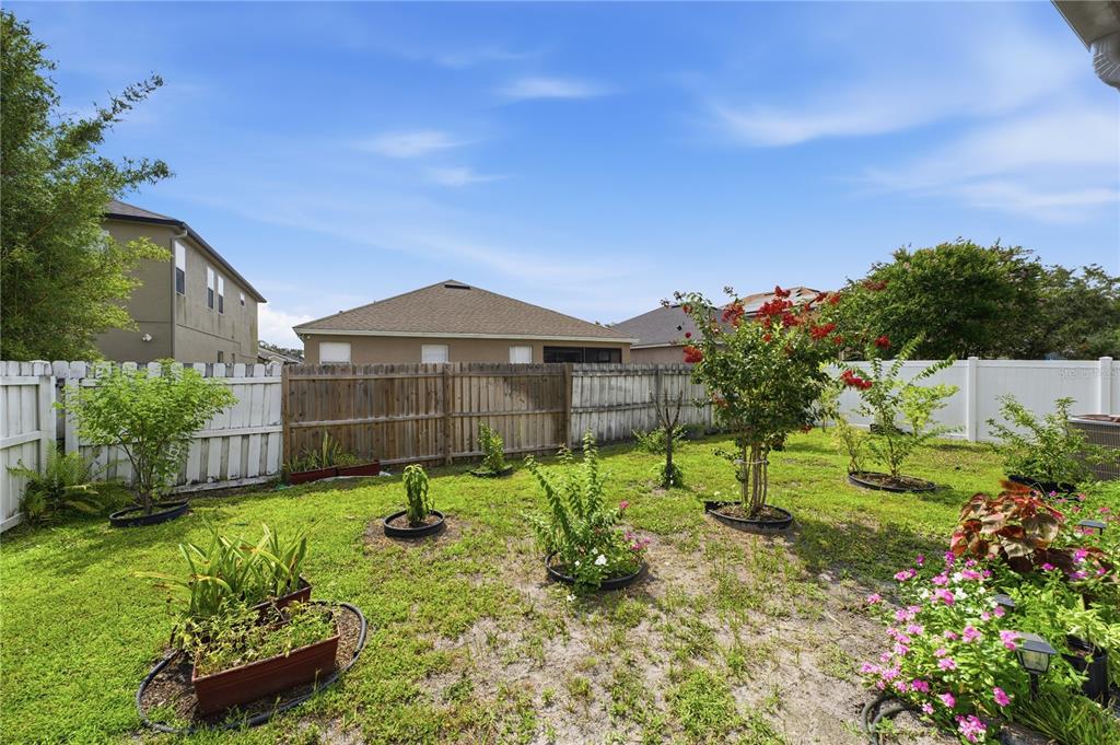 A backyard features a wooden fence, a white vinyl fence, and several small garden plants — 10114 OAK CREST ROAD, ORLANDO, FL