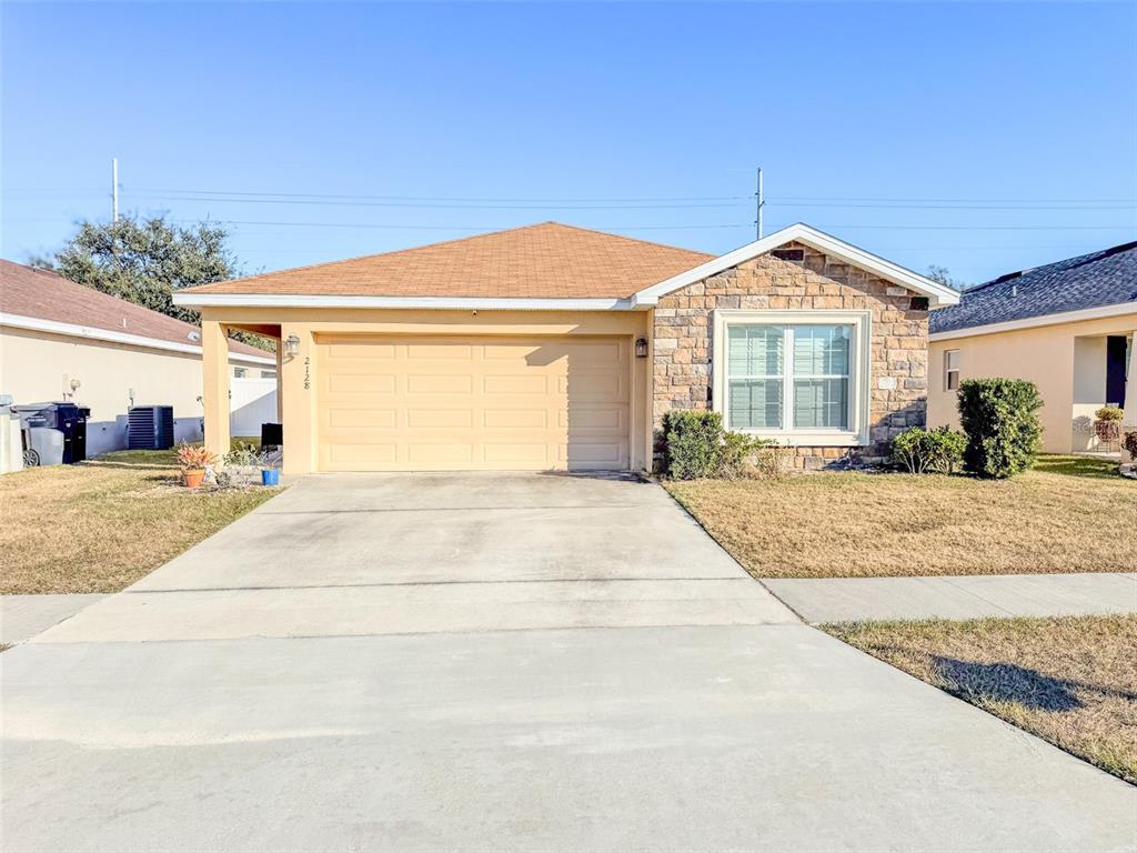 A single-story house with a tan stucco exterior, stone facade, and a two-car garage — 2128 BRETTON RIDGE BOULEVARD, WINTER HAVEN, FL