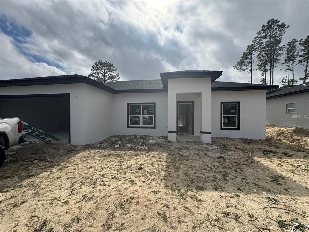 A newly constructed single-story house features white stucco walls, a dark roof, and an unfinished yard — 13449 SW 60TH AVENUE ROAD, OCALA, FL