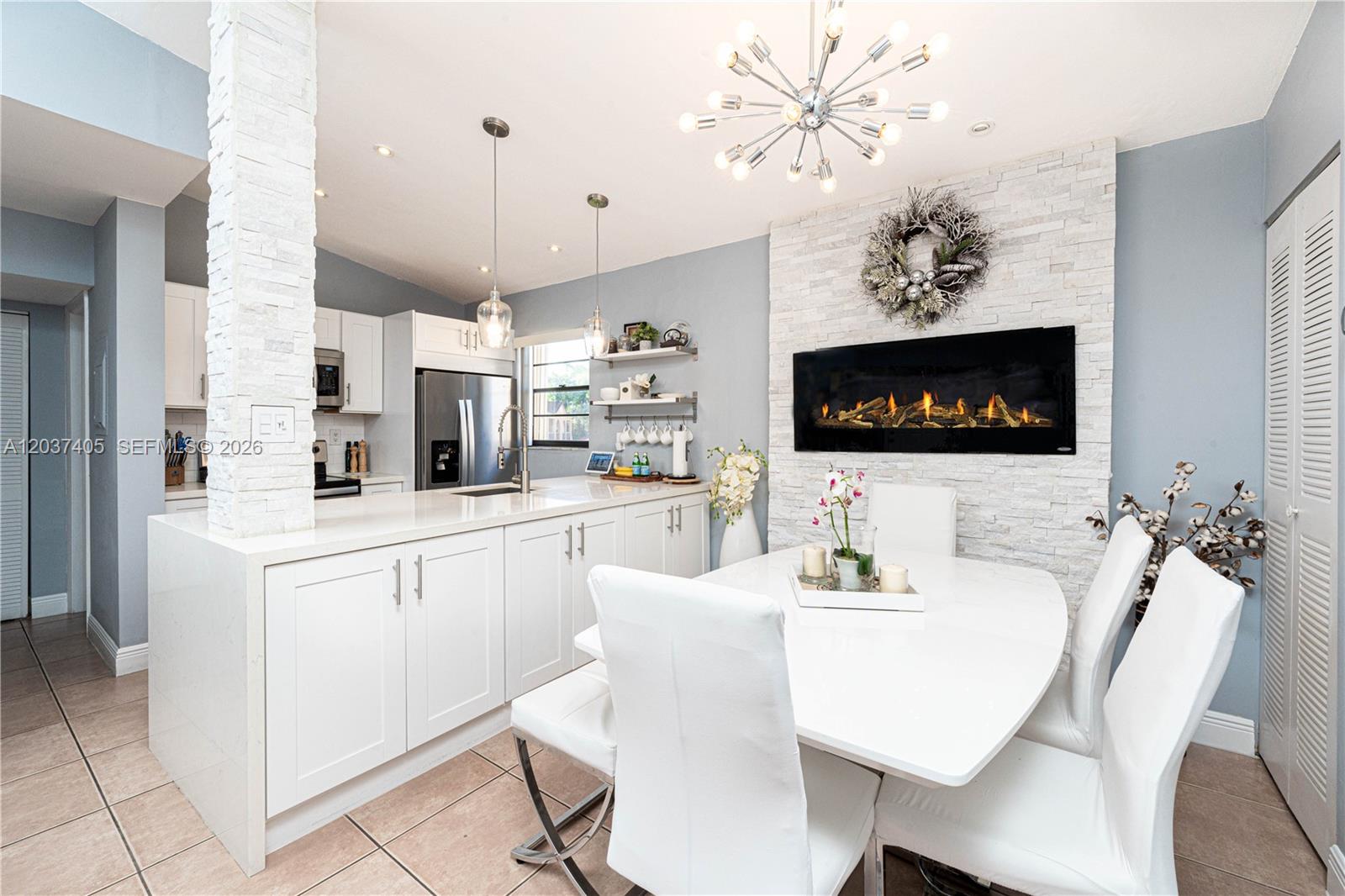 A modern kitchen and dining area features white cabinetry, a stone fireplace, and a chandelier — 18226 Mediterranean Blvd # 16, Hialeah FL 33015, HIALEAH, FL