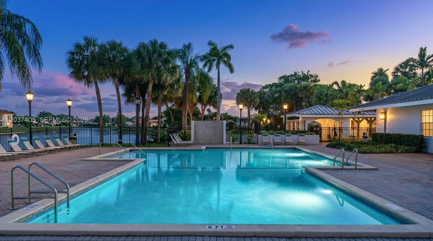 An outdoor swimming pool surrounded by a paved deck, palm trees, and a building exterior — 18226 Mediterranean Blvd # 16, Hialeah FL 33015, HIALEAH, FL