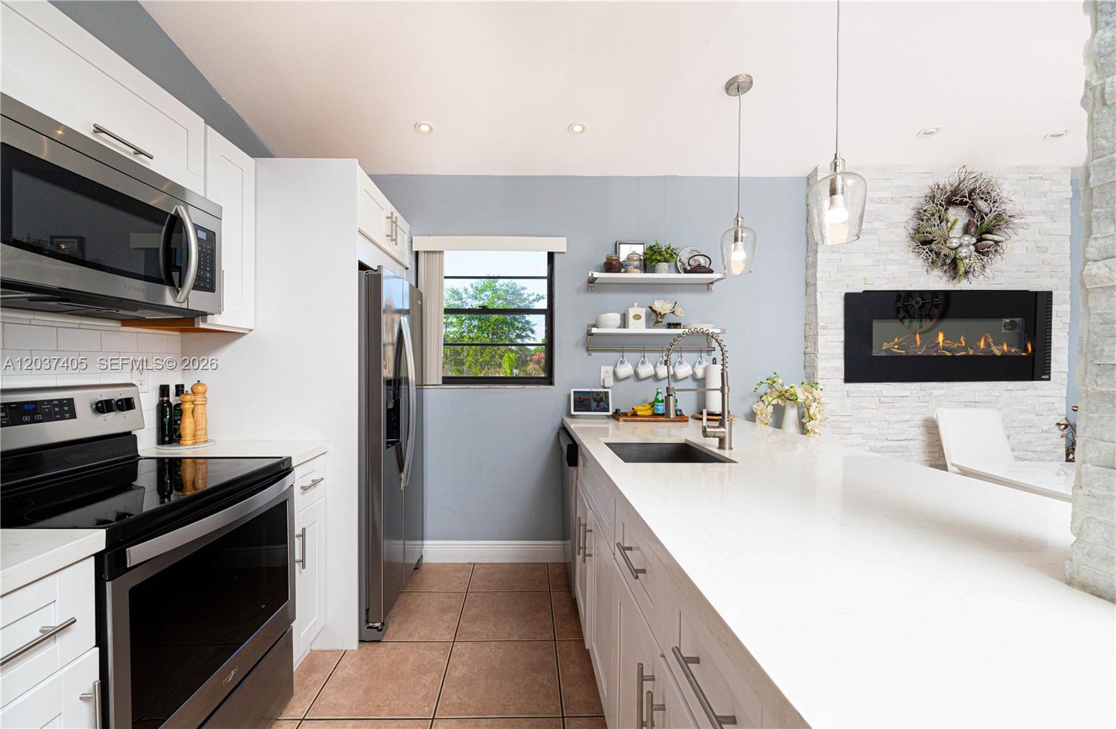 A modern kitchen features white cabinets, quartz countertops, stainless steel appliances, and a stone fireplace — 18226 Mediterranean Blvd # 16, Hialeah FL 33015, HIALEAH, FL
