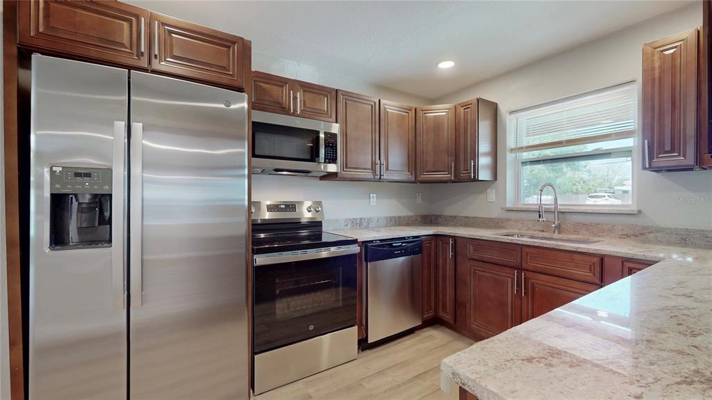 A kitchen features stainless steel appliances, dark wood cabinets, and light granite countertops — 505 FIELDER BOULEVARD, SEBRING, FL