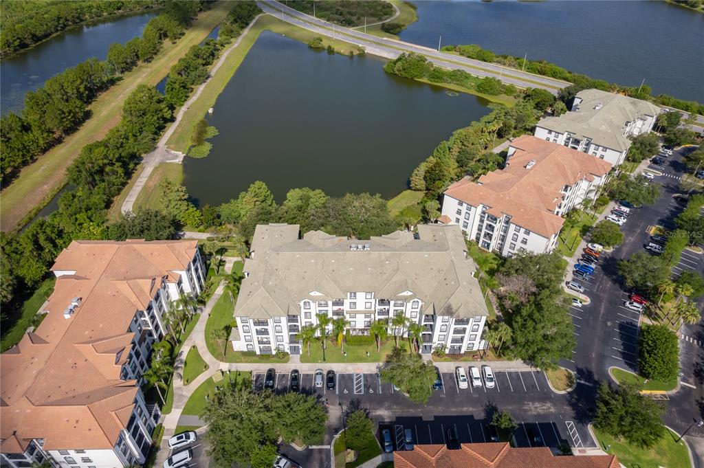 An aerial view shows apartment buildings with tan roofs surrounded by parking lots and a lake — 4102 BREAKVIEW DRIVE UNIT 40203, ORLANDO, FL