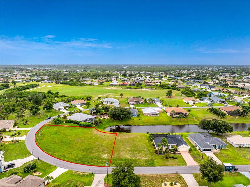 An aerial view shows a vacant, grass-covered residential lot outlined in red next to a pond — 19 MEDALIST PLACE, ROTONDA WEST, FL