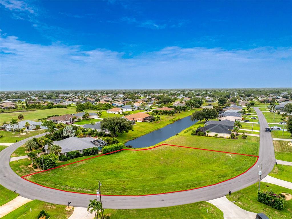 An aerial view shows a vacant, curved residential lot bordered by a road and a canal — 19 MEDALIST PLACE, ROTONDA WEST, FL