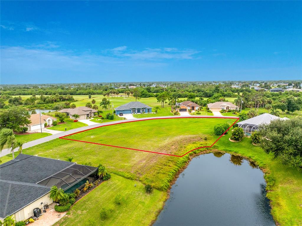 An aerial view shows a vacant, grass-covered residential lot outlined in red next to a pond — 19 MEDALIST PLACE, ROTONDA WEST, FL