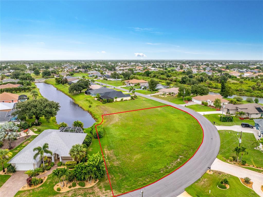 An aerial view shows a vacant, grass-covered residential lot bordered by a road and pond — 19 MEDALIST PLACE, ROTONDA WEST, FL