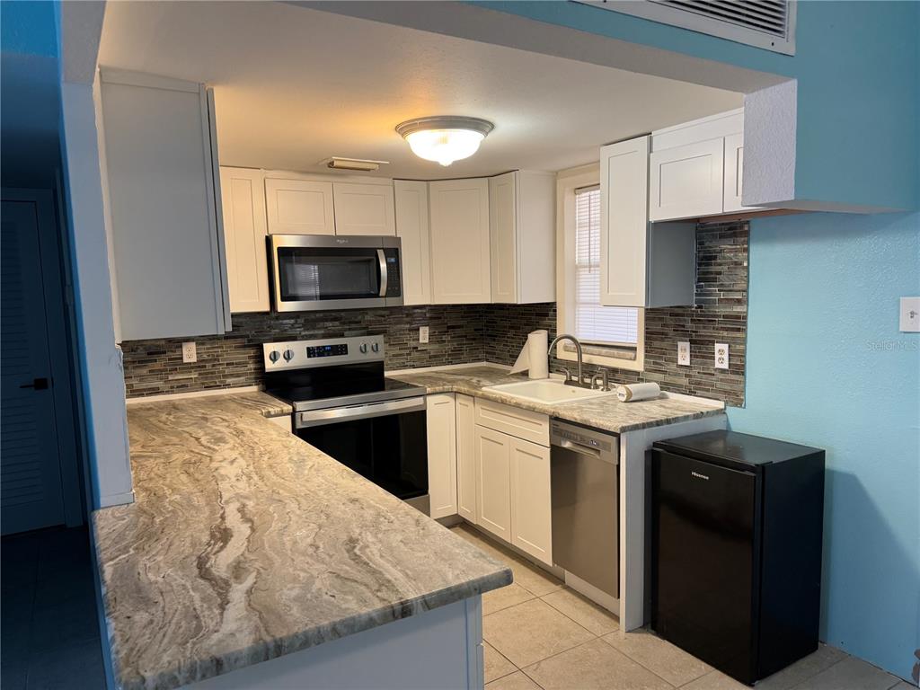 A kitchen features white cabinets, granite countertops, stainless steel appliances, and a tiled backsplash — 4515` MARINE PARKWAY UNIT 102, NEW PORT RICHEY, FL