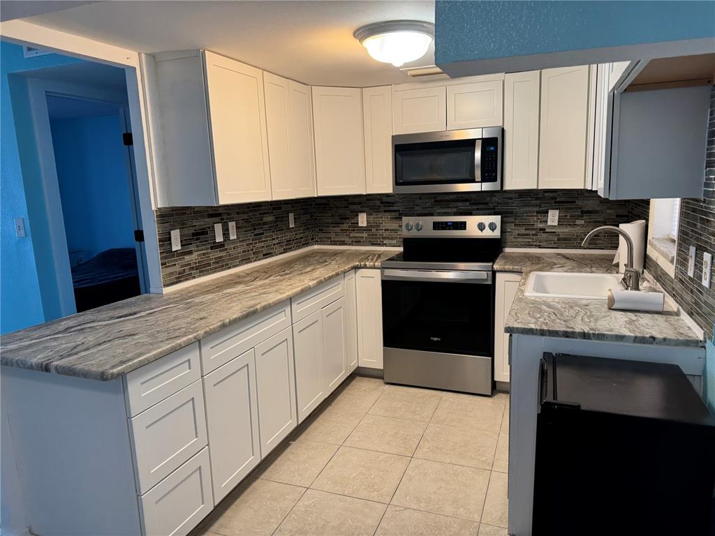 A kitchen features white cabinets, granite countertops, stainless steel appliances, and a tiled backsplash — 4515` MARINE PARKWAY UNIT 102, NEW PORT RICHEY, FL