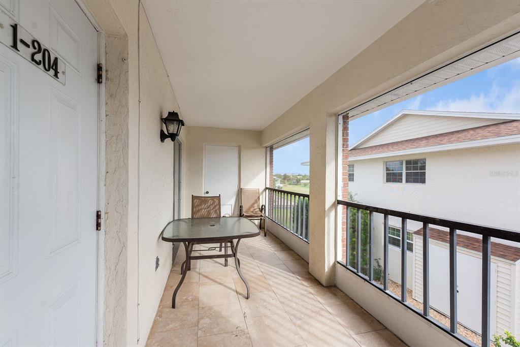 A covered balcony features a glass-top table, two chairs, tiled flooring, and a screened enclosure — 1531 PLACIDA ROAD UNIT 1-204, ENGLEWOOD, FL