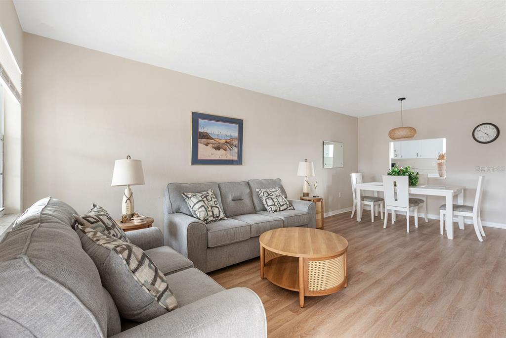 A living room and dining area with gray sofas, a round coffee table, and wood flooring — 1531 PLACIDA ROAD UNIT 1-204, ENGLEWOOD, FL