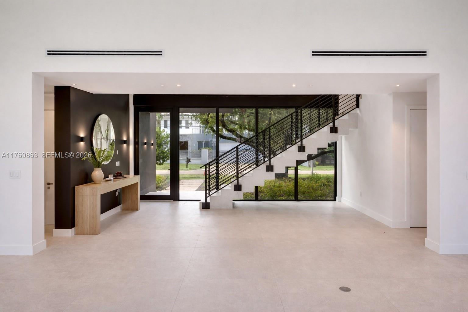 A modern foyer features a black accent wall, a wooden console table, and a floating staircase — 5921 SW 84th St, South Miami FL 33143, SOUTH MIAMI, FL
