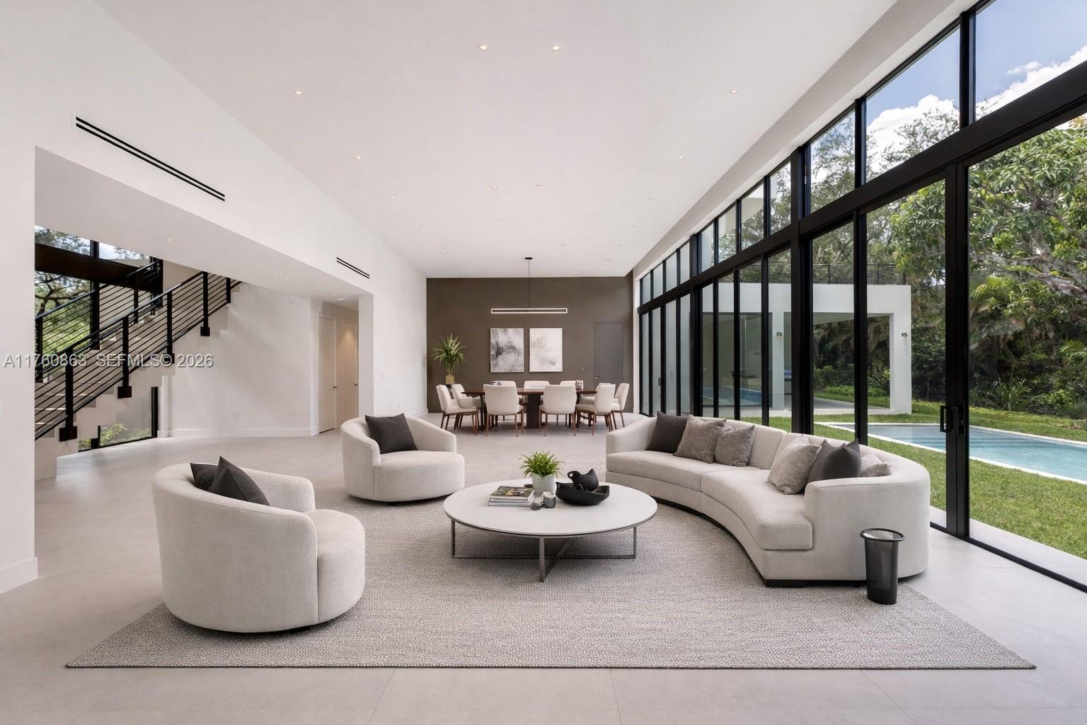 A modern living room features a curved sofa, two armchairs, and floor-to-ceiling windows overlooking a pool — 5921 SW 84th St, South Miami FL 33143, SOUTH MIAMI, FL