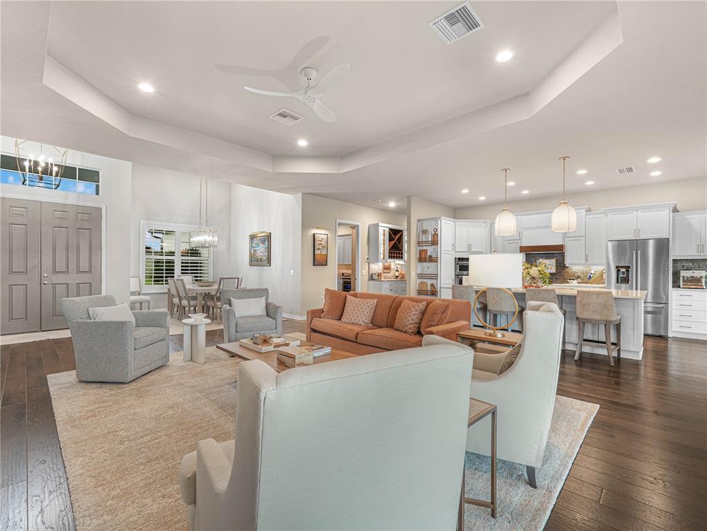 An open-concept living room and kitchen area with hardwood floors, a tray ceiling, and furniture — 6209 PINEHURST LOOP, WINTER HAVEN, FL