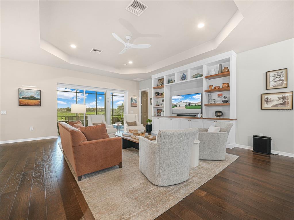 A living room features dark hardwood floors, a tray ceiling, and a large built-in media center — 6209 PINEHURST LOOP, WINTER HAVEN, FL