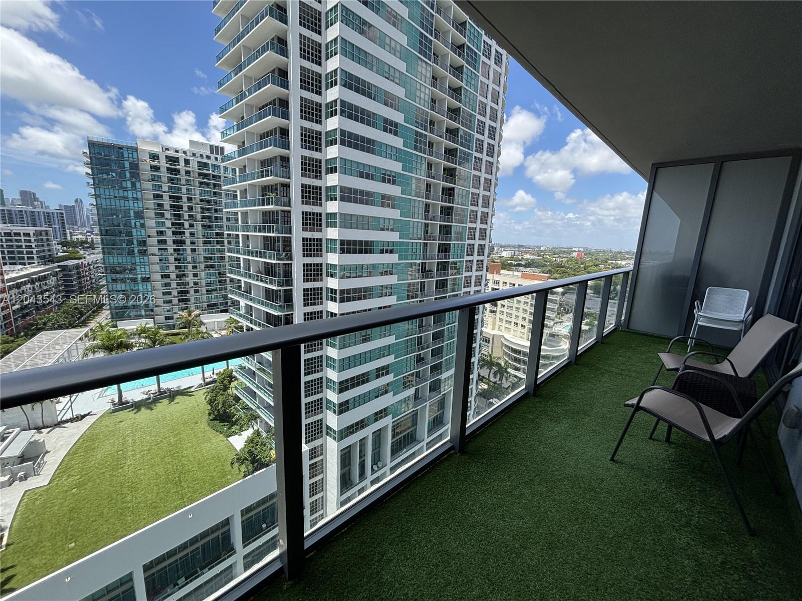 A balcony with artificial turf flooring features outdoor seating and views of neighboring high-rise buildings — 121 NE 34th St # 1703, Miami FL 33137, MIAMI, FL