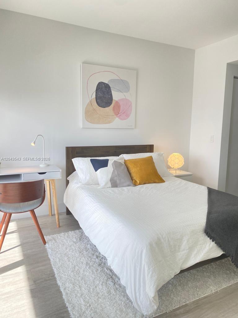 A bedroom features a bed with white bedding, a wooden headboard, and a small desk — 121 NE 34th St # 1703, Miami FL 33137, MIAMI, FL
