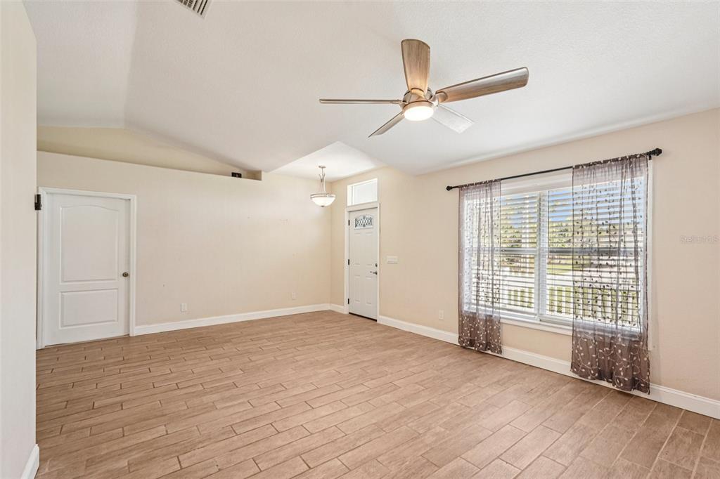 An open-concept living room and kitchen feature light-colored walls, wood-look tile flooring, and white cabinetry — 1929 NORVELL AVENUE, NORTH PORT, FL