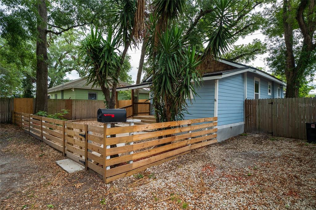 A blue house with a wooden fence and a mailbox in a gravel yard — 6704 N TALIAFERRO AVENUE, TAMPA, FL