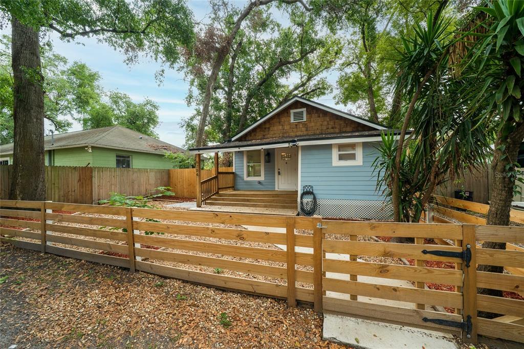 A light blue house with a wooden porch and fence stands behind a gravel yard — 6704 N TALIAFERRO AVENUE, TAMPA, FL