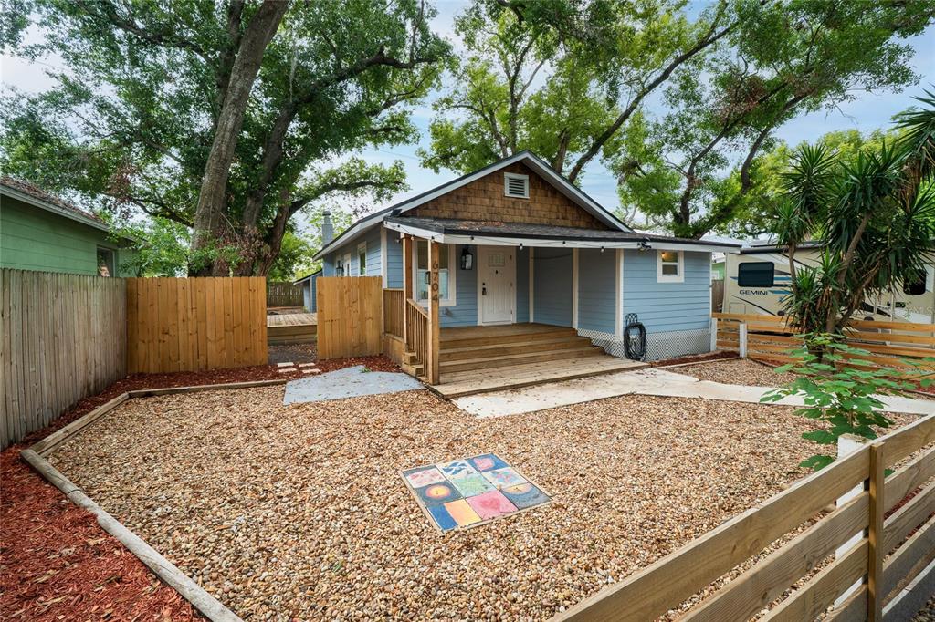 A light blue house with a wooden porch and gravel yard sits behind a fence — 6704 N TALIAFERRO AVENUE, TAMPA, FL