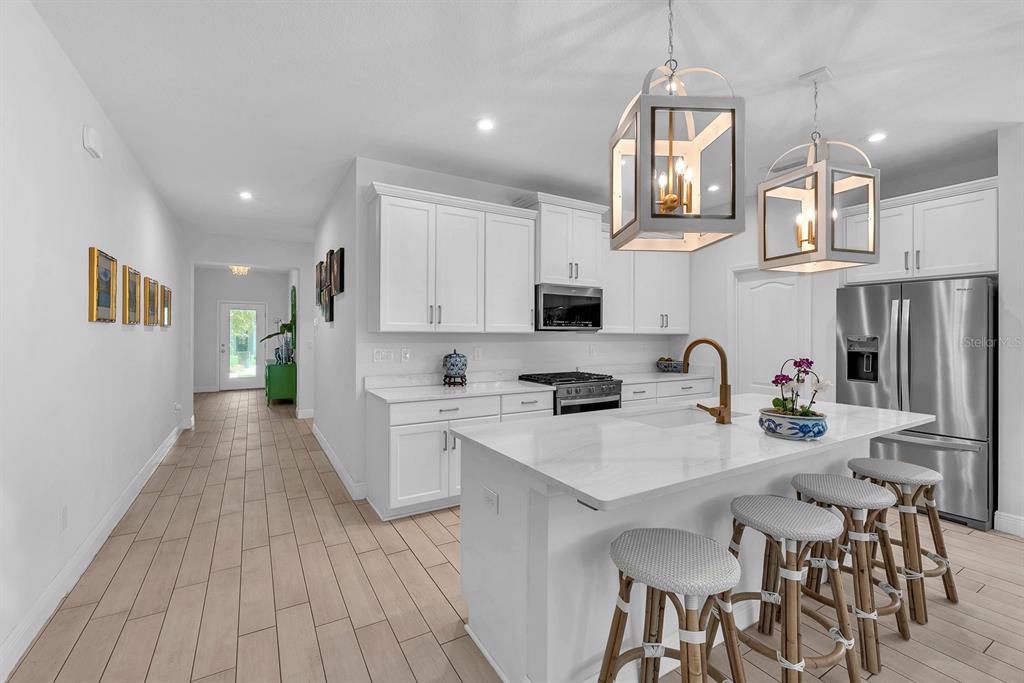 A modern kitchen features white cabinetry, a marble-topped island with bar stools, and pendant lighting — 14115 CARISSA MEADOWS COURT, RIVERVIEW, FL