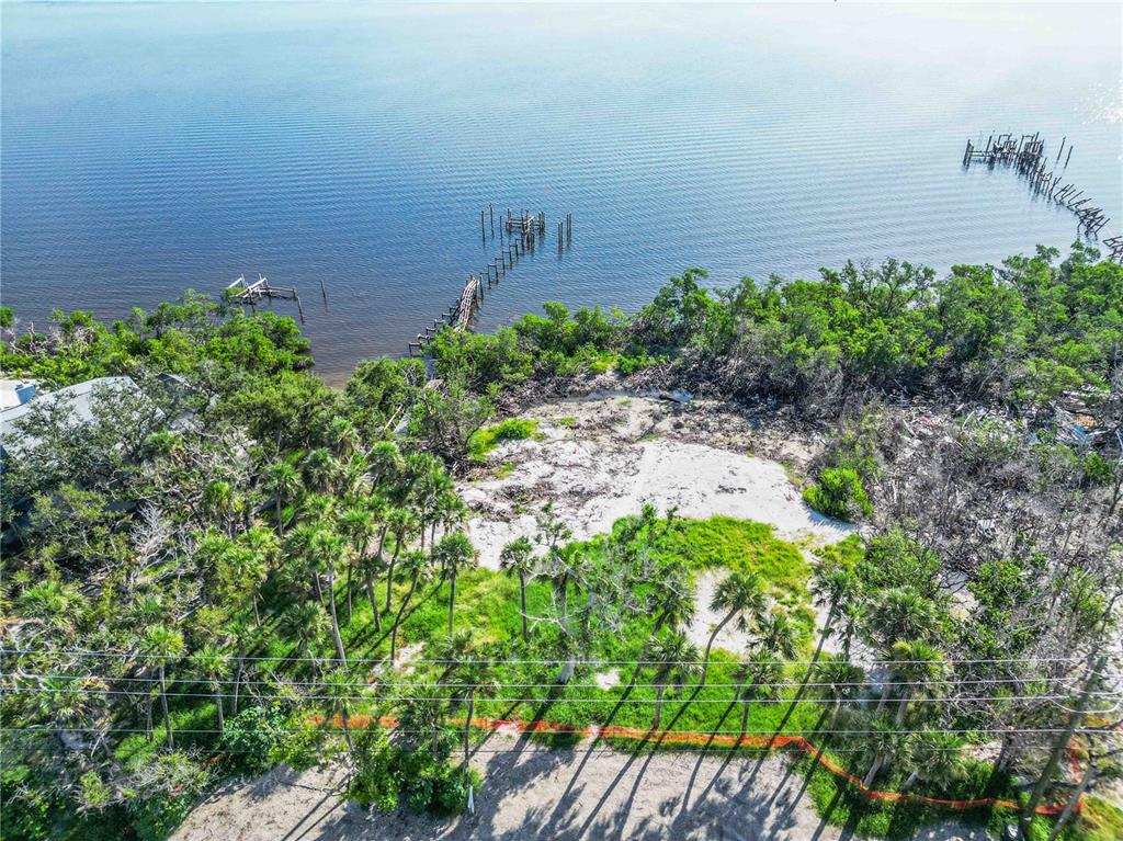 An aerial view of a waterfront lot featuring palm trees, vegetation, and two wooden piers — 6845 MANASOTA KEY ROAD, ENGLEWOOD, FL