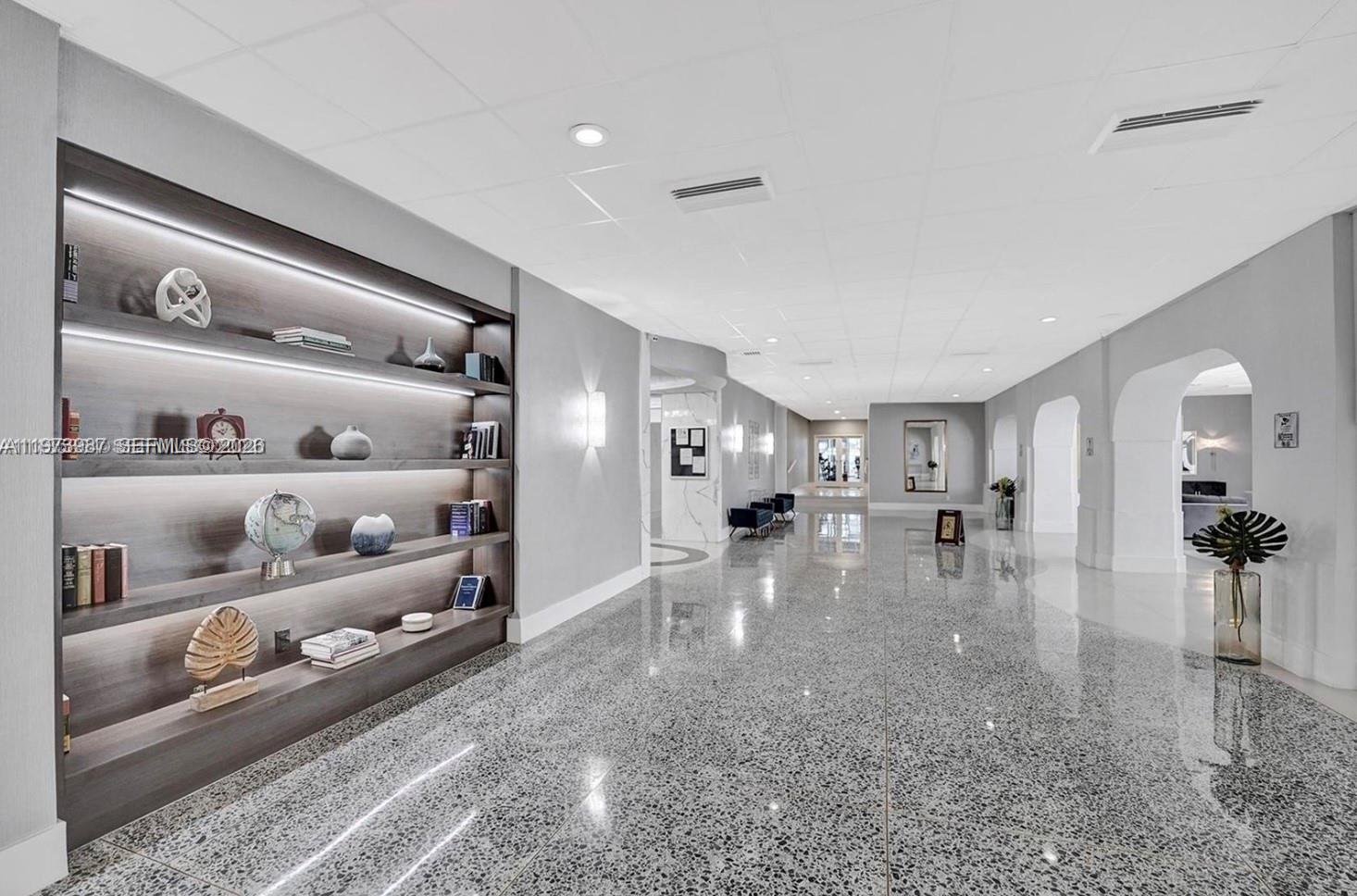 A long, modern hallway features a large built-in display shelf and polished terrazzo flooring — 3140 S Ocean Dr # 1812, Hallandale Beach FL 33009, HALLANDALE BEACH, FL