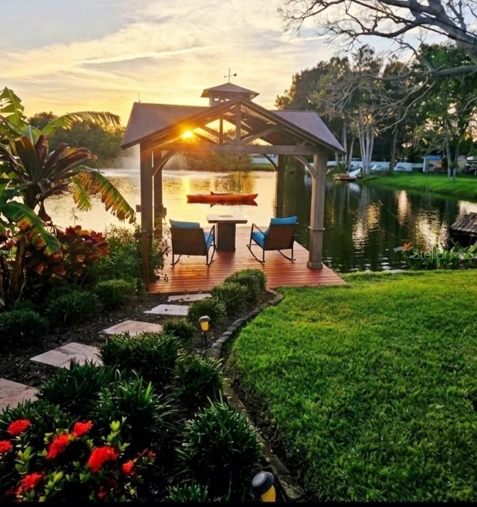 A wooden gazebo with two chairs sits on a deck overlooking a lake at sunset — 5564 N 63RD WAY N, ST PETERSBURG, FL