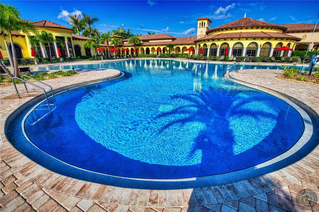 A large, circular swimming pool with a palm tree mosaic sits before a Mediterranean-style clubhouse — 12355 GHIBERTI CIRCLE UNIT 101, VENICE, FL