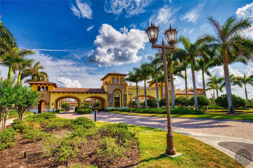 A gated community entrance features a yellow stucco building with arched driveways and palm trees — 12355 GHIBERTI CIRCLE UNIT 101, VENICE, FL