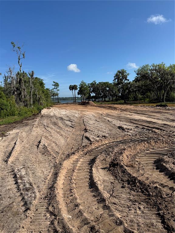 A cleared dirt lot with tire tracks leads toward a lake surrounded by trees — Lot K4 BLUE HERON CIRCLE, DEER ISLAND, FL