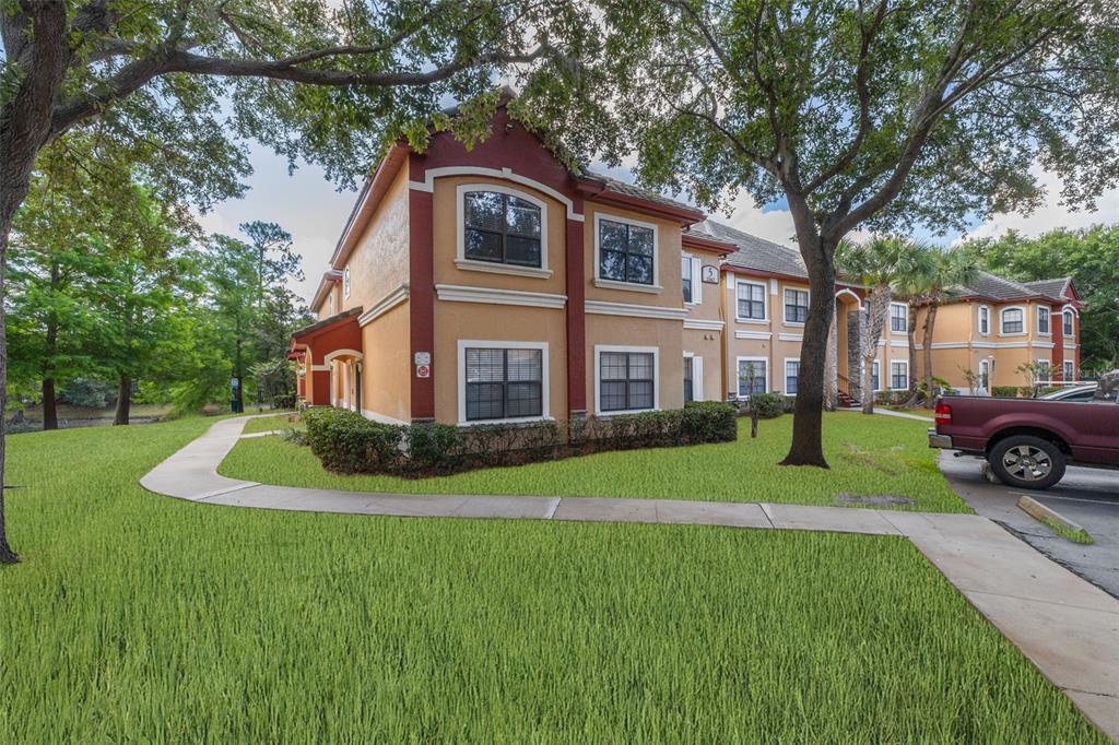 A sidewalk leads past a building exterior toward a pond with a fountain and trees — 2262 CHIANTI PLACE UNIT 5-0511, PALM HARBOR, FL