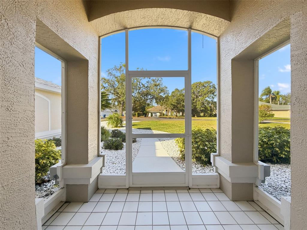 A tiled entryway features a white screen door looking out onto a landscaped front yard — 9428 APPLE DUMPLING COURT, WEEKI WACHEE, FL