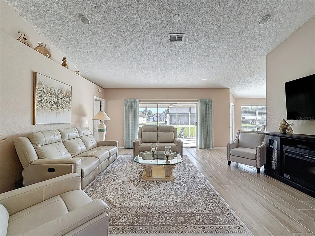 A living room features light-colored leather furniture, a patterned area rug, and a sliding glass door — 9428 APPLE DUMPLING COURT, WEEKI WACHEE, FL