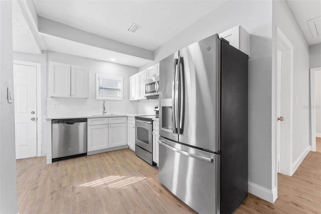 A kitchen features stainless steel appliances, white cabinetry, and light wood-look flooring — 1927 13TH STREET S, ST PETERSBURG, FL