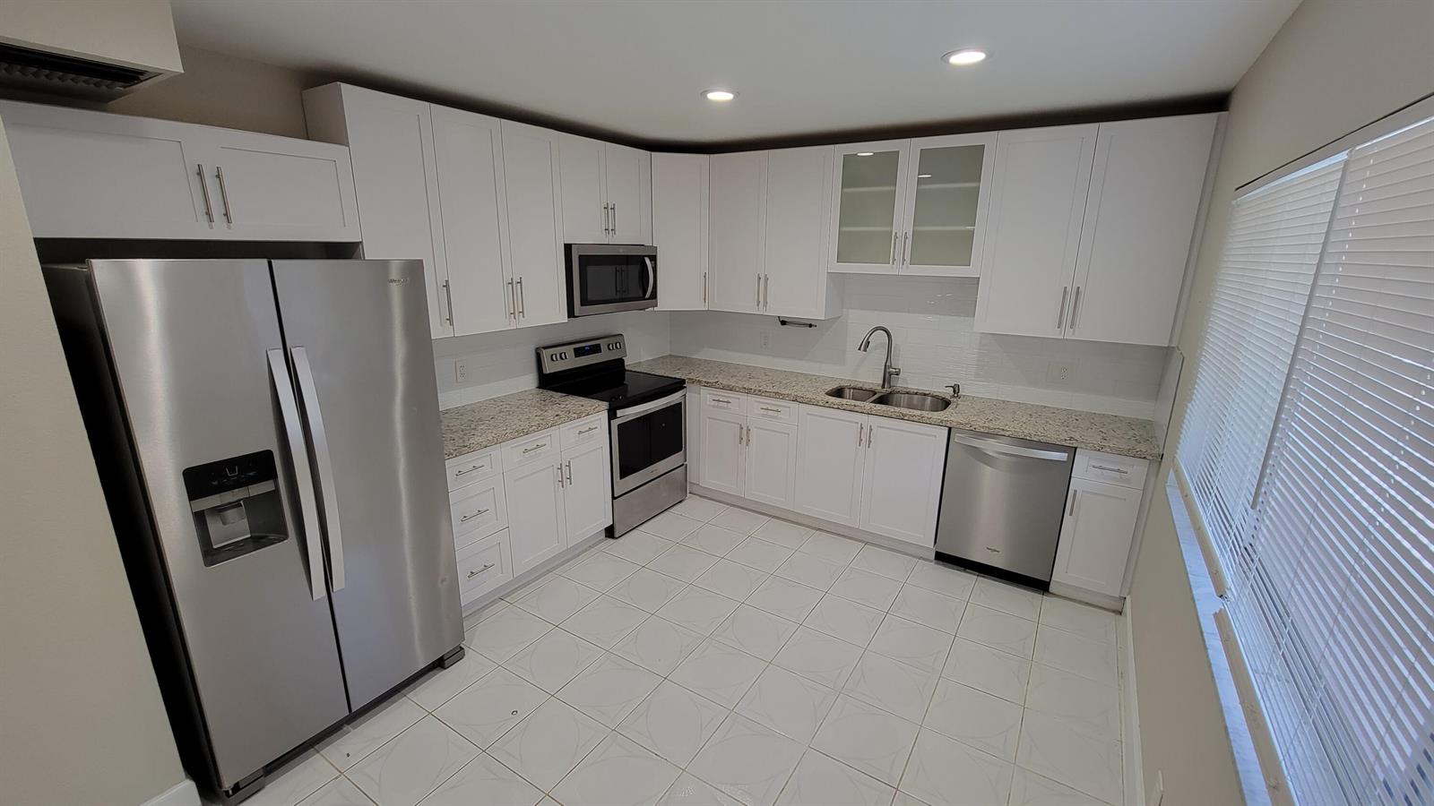 A kitchen features white cabinets, stainless steel appliances, granite countertops, and white tile flooring — 6289 Lear Drive # 203, Lake Worth FL 33462, LAKE WORTH, FL