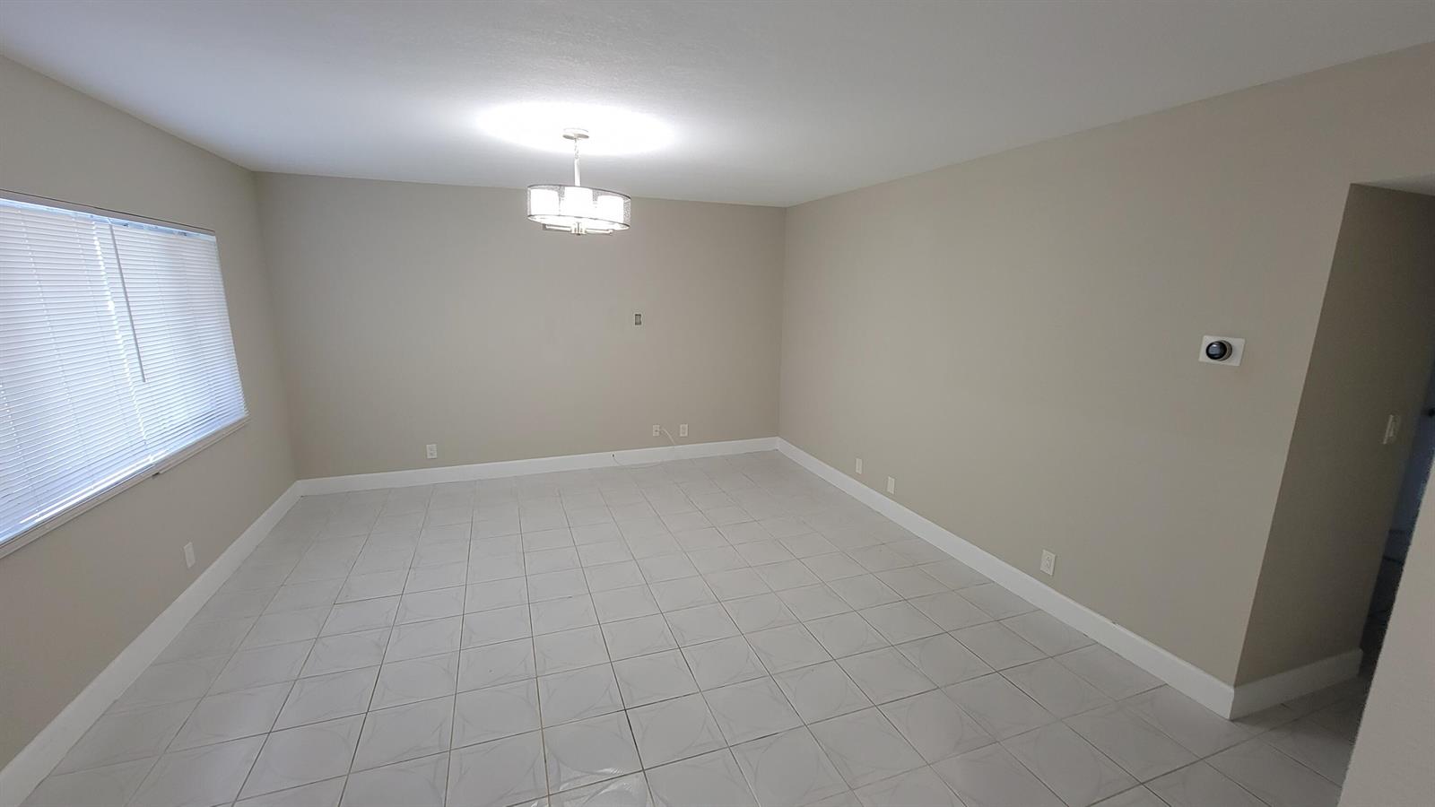 An empty room with light-colored tile flooring, beige walls, a chandelier, and a window — 6289 Lear Drive # 203, Lake Worth FL 33462, LAKE WORTH, FL