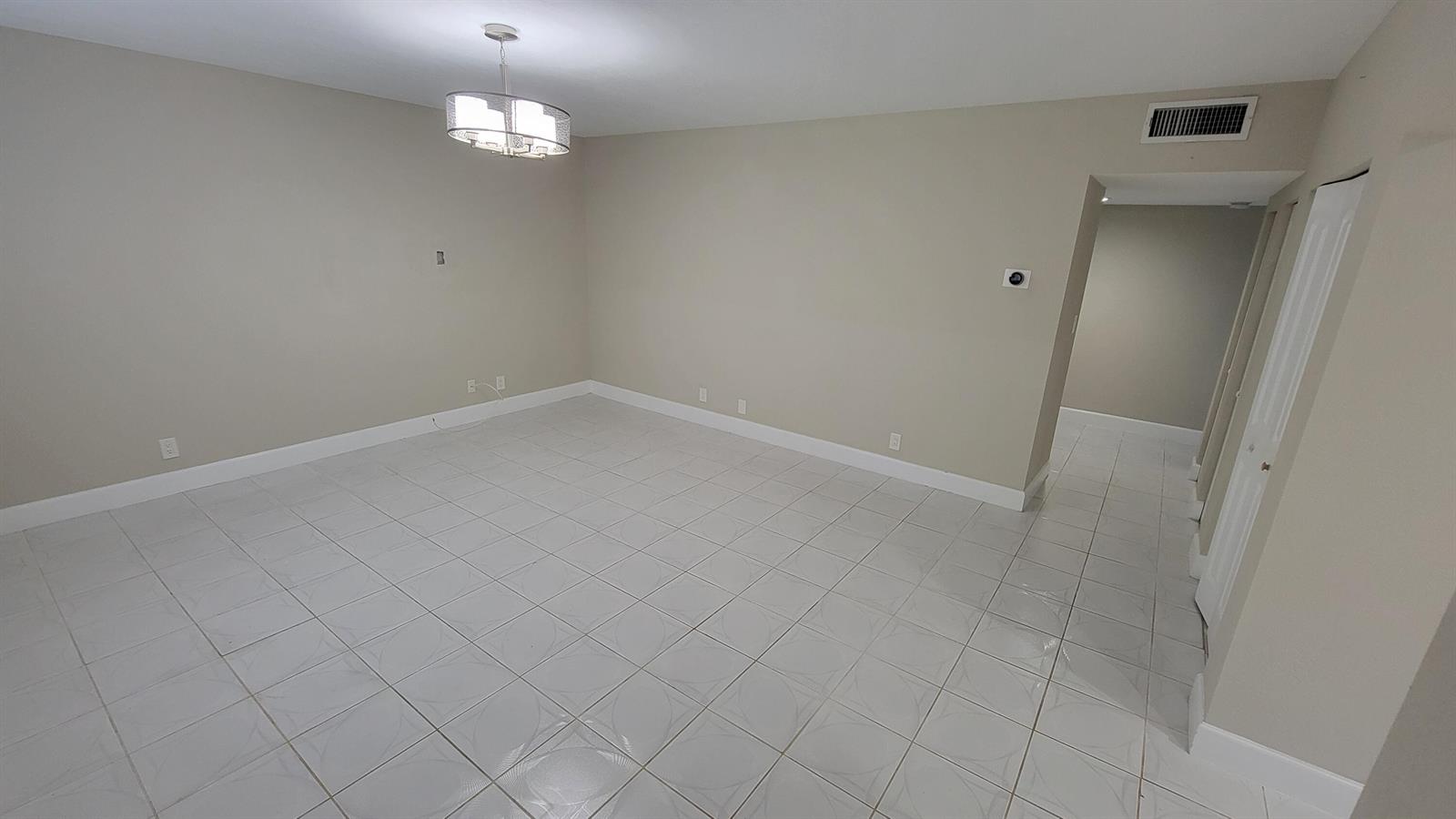 An empty room features light-colored tile flooring, beige walls, and a modern chandelier — 6289 Lear Drive # 203, Lake Worth FL 33462, LAKE WORTH, FL