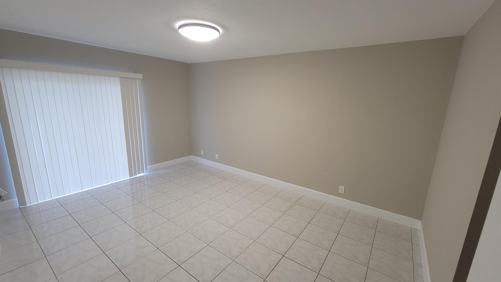 An empty room features light-colored tile flooring, beige walls, and a sliding glass door — 6289 Lear Drive # 203, Lake Worth FL 33462, LAKE WORTH, FL